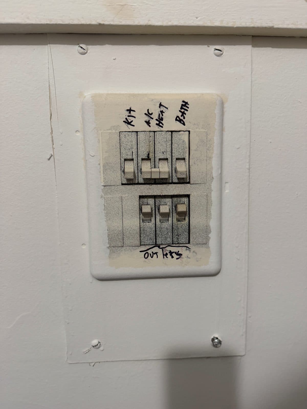 A small apartment breaker panel with the breakers and cover painted over, the circuits marked by hand for the kitchen, air conditioning, heat, bath and outlets