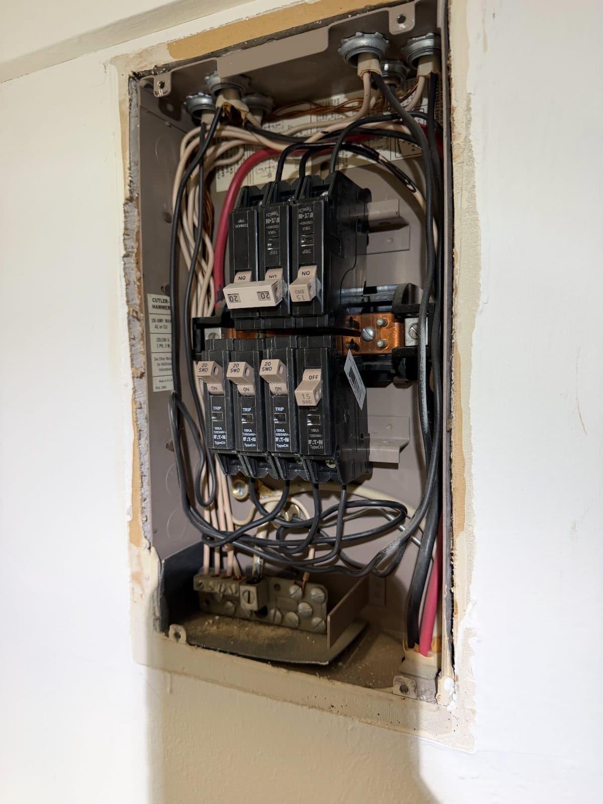 An apartment load center opened up in the wall, its breakers and wiring exposed during a breaker replacement job