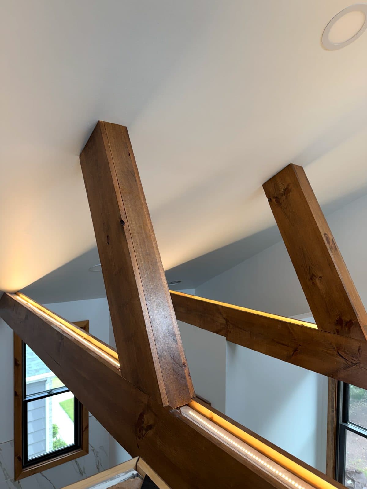 Warm LED strip lighting set into the tops of wood ceiling beams under a vaulted ceiling