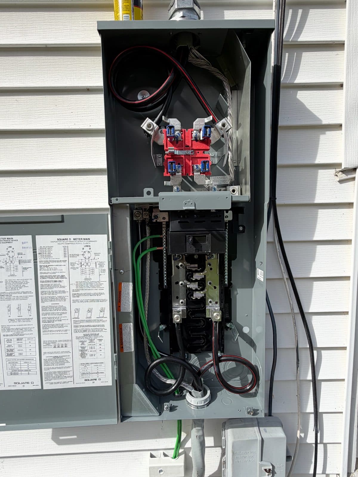 A meter main combo open on the side of a Berlin house, with the new main breaker and service wiring landed inside