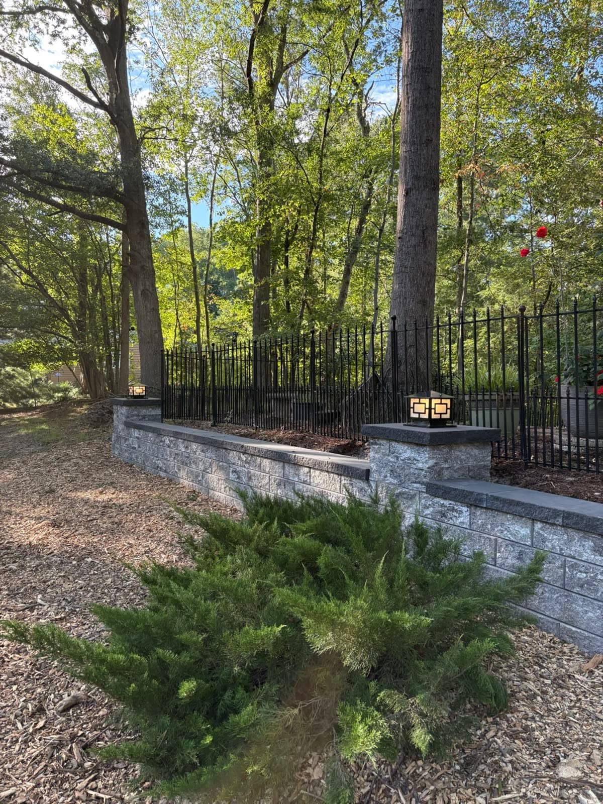 Warm pillar lights on a stone retaining wall beside a black iron fence, wired by Stagg Electric